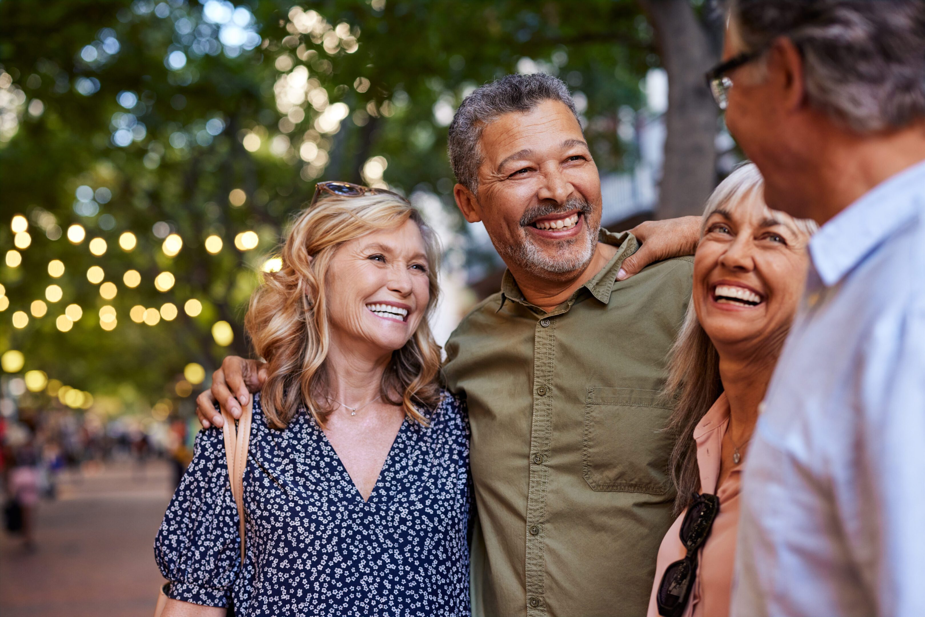Three friends smiling and enjoying a moment outdoors with blurred lights in the background.