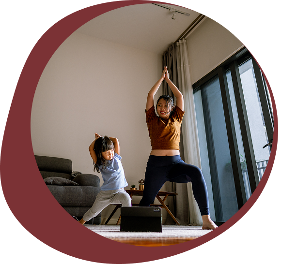Mother and daughter doing yoga poses together in a sunlit living room.