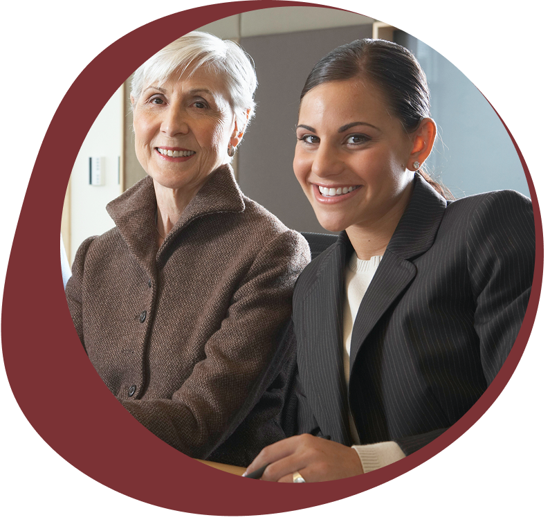 Two professional women, one older and one younger, smiling together in a business setting.