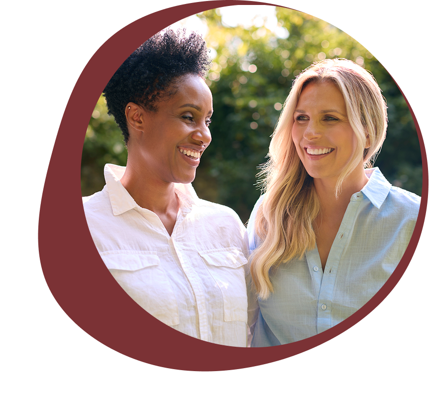 Two women smiling and talking outdoors in sunlight.